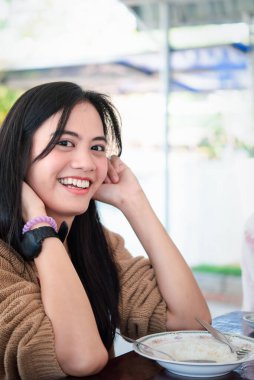 Asyalı, sevimli, Tayland yemeği ve pilav yiyen bir kadın restorandaki yemek masasında mutlu ve duygusal bir şekilde yemek yiyor.