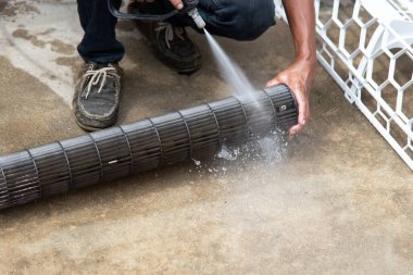 Bakım hizmeti sırasında müşteri evindeki duvardaki tozu temizlemek için havalandırma soğutucusunu suyla temizleyen işçiden işçiye.