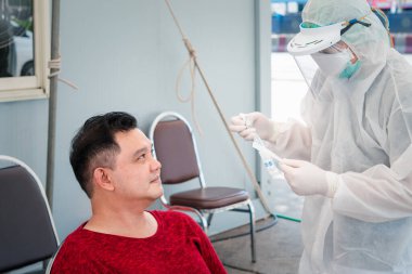 PPE kostümlü doktor ve COVID-19 tarafından kontrol edilen Asyalı hasta nazofaringeal veya orofaringeal temizleme yapıyor.