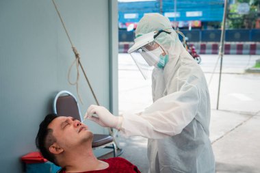 PPE kostümlü doktor ve COVID-19 tarafından kontrol edilen Asyalı hasta nazofaringeal veya orofaringeal temizleme yapıyor.