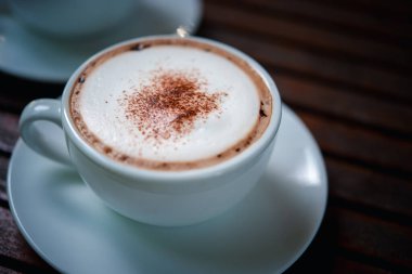 Kafe veya restoranda müşterilere servis yapmak için ahşap masadaki beyaz kahve fincanındaki kahve içeceği.