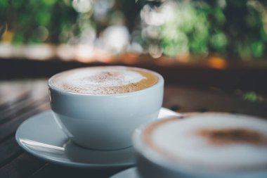 Kafe veya restoranda müşterilere servis yapmak için ahşap masadaki beyaz kahve fincanındaki kahve içeceği.