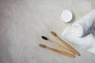 Bambu diş fırçaları, beyaz pamuk havlu ve açık gri arka planda dişlerini kasede fırçalamak için pudra. Plastik yok, sıfır atık kavramı.