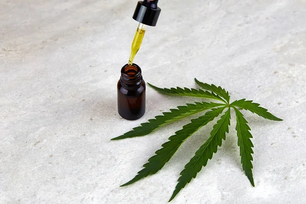 Bir kenevir yaprağı ve küçük bir şişe esrar. CBD yağlı kozmetik ürünleri. Düzlük, minimalizm. 