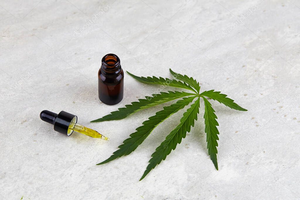 A cannabis leaf and a small bottle of cannabis. Cosmetics with CBD oil. Flat lay, minimalism. 