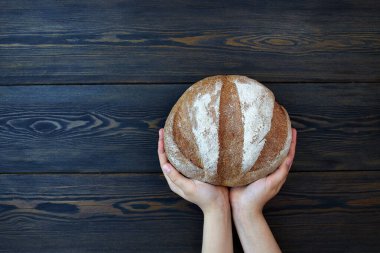 Koyu ahşap arka planda bir çocuğun ellerinde yuvarlak bir somun taze ekmek..