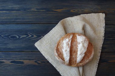 Koyu ahşap arka planda keten peçeteyle taze ekmeğin yuvarlak somunu..
