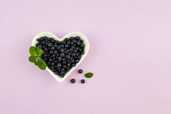 Blueberries in bowl in the shape of a heart on a lilac background