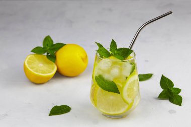 Buzlu ve naneli limonlu soğuk limonata. Gri arka planda metal kamışla yaz kokteylini tazeliyorum..