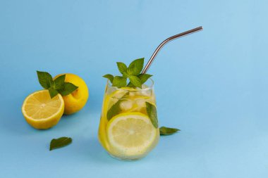 Buzlu limonlu soğuk limonata. Mavi arka planda metal pipetle yaz kokteylini tazeliyorum..