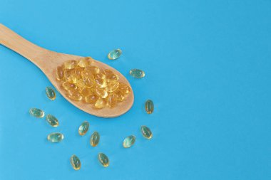 Mavi arka planda tahta kaşıkta balık yağı ya da omega kapsülleri..
