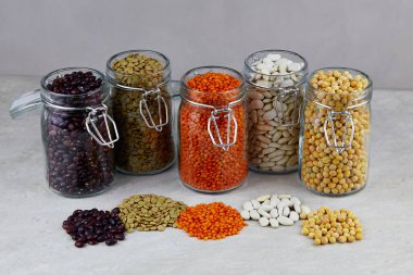 Cam kaselerdeki farklı kurumuş baklagiller: kırmızı mercimek, yeşil mercimek, bezelye, kırmızı fasulye, gri arkaplanda beyaz fasulye