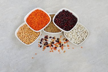 Seramik kaselerde farklı kurumuş baklagiller: kırmızı mercimek, yeşil mercimek, bezelye, kırmızı fasulye, gri arka planda beyaz fasulye