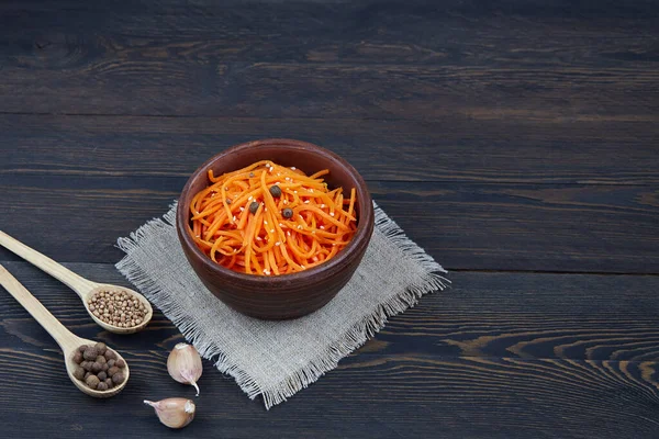 Sarımsaklı ve kişniş soslu Kore havuç salatası. Koyu ahşap arka planda seramik bir kasede ızgara çiğ havuç..