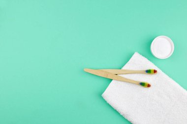 Bambu diş fırçaları, beyaz pamuk havlu ve yeşil arka planda dişlerini kasede fırçalamak için pudra. Plastik yok, sıfır atık kavramı.
