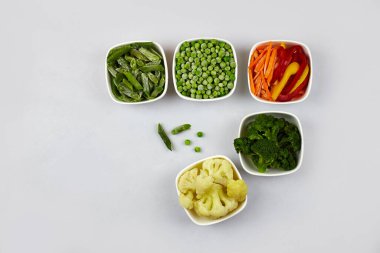 Donmuş sebzeler: brokoli, çalı fasulyesi, karnabahar, biber, yeşil bezelye ve gri arkaplanda havuç. Kopyalama alanı olan üst görünüm.