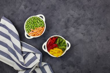 Donmuş sebzeler: Çalı fasulyesi, biber, yeşil bezelye ve koyu gri arka planda havuç. Kopyalama alanı olan üst görünüm.