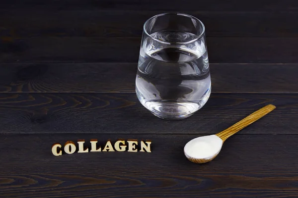 Collagen protein powder in spoon and a glass of water  on dark wooden  background. Natural beauty and health supplement for skin, bones, joints.