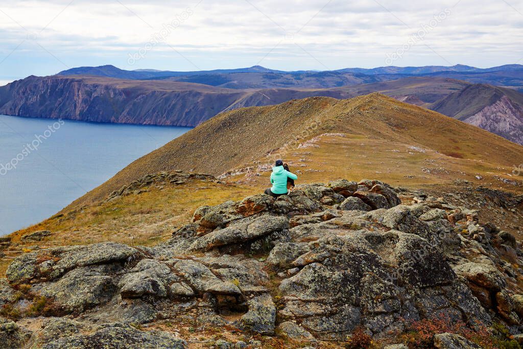 Beautiful autumn view of lake Baikal. A young woman with a dog in the background admiring the Bay of Baikal.