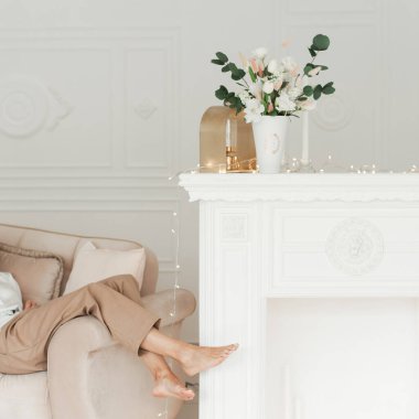 İç kısımda yapay çiçekler var. İç kısımda dekoratif çiçekler var. Vazodaki yapay çiçekler. Odanın içi bembeyaz. Dekoratif şömine. Seksi bacaklar.. 