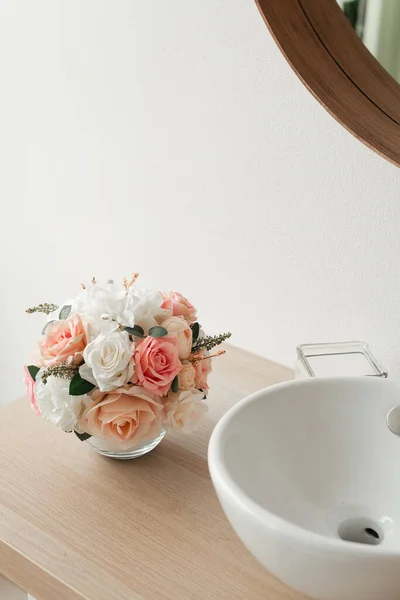 Artificial flowers in the bathroom interior. Decorative flowers in a round vase. Artificial flowers in a round vase. White bathroom interior. Decorative flowers.