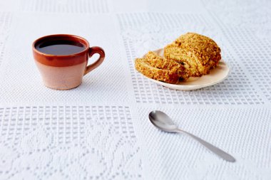 a brown mug with coffee on a white tablecloth, a sweet roll on the plate