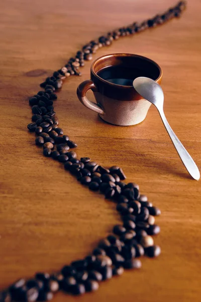 the brown mug stands on a wooden table, the coffee beans are laid out with a curve line