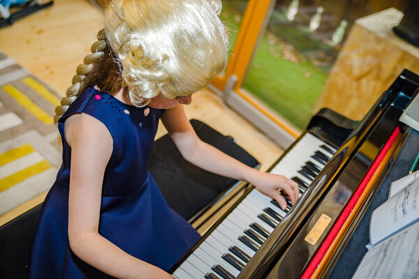 Cute little girl playing piano, dressing in retro Mozart periwig, indoor