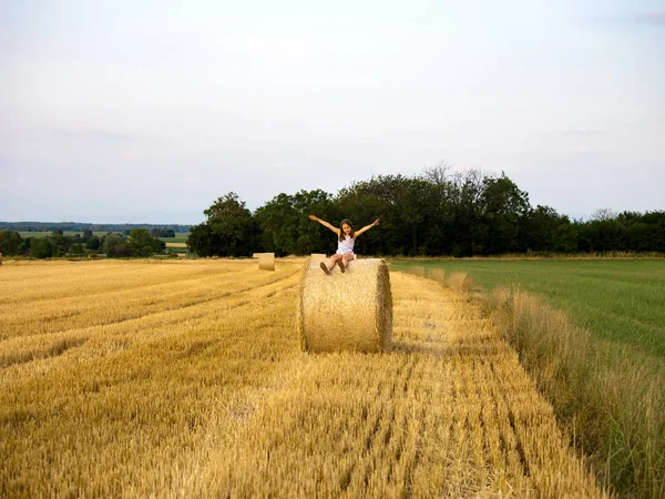 La petite fille est assise sur une meule de foin au crépuscule du jour — Photo