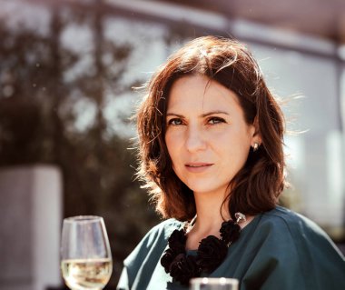 Restoranın açık terasında elinde bir bardak şarapla güzel bir genç kadın.