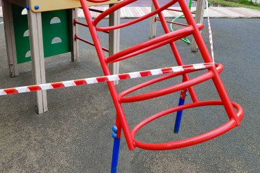 Oyun parkındaki çocuk spor binası kırmızı bant ile sarılmış. Açık havada yürüyüş yasağı, koronavirüs gribi virüsünün biyolojik tehlikesinin önlenmesi. Alarm durumu.