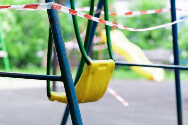 Parktaki sarı çocuk salıncağı kırmızı bariyer bandıyla sarılmış. Dışarı çıkın. Açık havada yürüyüş yasağı, Coronavirus gribi virüsünün önlenmesi covid-19. Park kapandı. seçici odak