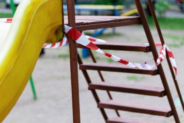 Çocuk parkındaki merdivenli bir kaydırak kırmızı bariyer bandıyla sarılmış. Açık havada yürüyüş yasağı, Coronavirus gribi virüsünün önlenmesi covid-19. Salgın. seçici odak