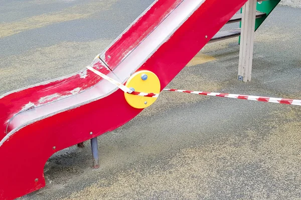 赤いバリアテープで包まれた公園の遊び場に子供たちが乗るための金属スライド 屋外散歩の禁止 コロナウイルスインフルエンザの生物学的危険の防止 — ストック写真