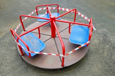 Oyun parkındaki kırmızı atlıkarınca bariyer bandıyla sarılmış. Açık havada. Dışarıda yürüyüş yasağı, koronavirüs gribi virüsü Covid-19 'un biyolojik tehlikesinin önlenmesi. Evde kal.