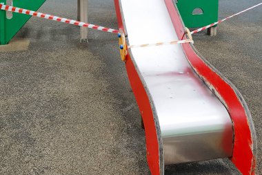 Kırmızı metal kaydırak çocukların parktaki oyun parkında kırmızı bariyer bandıyla gezmeleri için. Dışarı çıkın. Açık havada yürüyüş yasağı, Coronavirus gribi virüsünün önlenmesi covid-19.