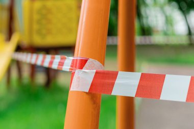 Parktaki yeşil çimlerin üzerinde kırmızı bariyer bandıyla sarılı çocuk parkı. Dışarı çıkın. Açık havada yürüyüş yasağı, Coronavirus gribi virüsünün önlenmesi covid-19. seçici odak