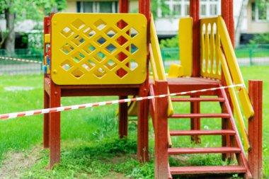 Parktaki çocukların eğlencesi için sarı bir slayt kırmızı bariyer bandıyla sarılmış. Açık havada yürüyüş yasağı, Coronavirus gribi virüsünün önlenmesi covid-19. Uyarı. seçici odak