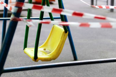 Sarı çocuk salıncağı parktaki bir spor sahasında kırmızı bariyerlerle sarılı. Açık havada yürüyüş yasağı, Coronavirus gribi virüsünün önlenmesi covid-19. Güvenlik. seçici odak