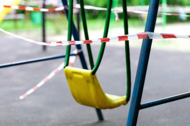 Sarı metal çocuk salıncağı parktaki bir spor sahasında kırmızı bariyer bandıyla sarılı. Açık havada yürüyüş yasağı, Coronavirus gribi virüsünün önlenmesi covid-19. seçici odak