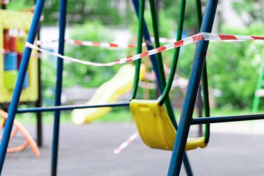 Sarı çocuk salıncağı parktaki bir spor sahasında kırmızı bariyerlerle sarılı. Açık havada yürüyüş yasağı, Coronavirus gribi virüsünün önlenmesi covid-19. Korumak. seçici odak