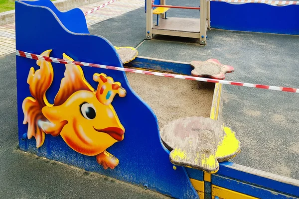 Parktaki çocuk parkında kırmızı bant ile sarılı bir çocuk kum havuzu. Açık havada. Açık havada yürüyüş yasağı, Coronavirus gribi virüsünün önlenmesi covid-19. virüs salgını.