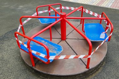 Oyun parkındaki kırmızı atlıkarınca bariyer bandıyla sarılmış. Açık havada. Dışarıda yürüyüş yasağı, koronavirüs gribi virüsü Covid-19 'un biyolojik tehlikesinin önlenmesi. park kapalı