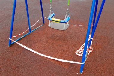 Çocukların mavi salıncağı, kırmızı bariyerlerle sarılı bir spor sahasında. Açık havada yürüyüş yasağı, koronavirüs gribi virüsünün biyolojik tehlikesinin önlenmesi. uzak durma işareti.
