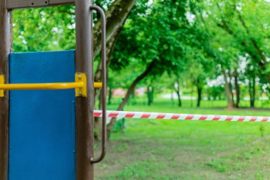 Parktaki yeşil çimlerin üzerinde kırmızı bariyer bandıyla sarılı çocuk parkı. Açık havada yürüyüş yasağı, Coronavirus gribi virüsünün önlenmesi covid-19. Corona virüsü. seçici odak