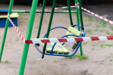 Sarı çocuk salıncağı parktaki bir spor sahasında kırmızı bariyerlerle sarılı. Dışarı çıkın. Açık havada yürüyüş yasağı, Coronavirus gribi virüsünün önlenmesi covid-19. seçici odak