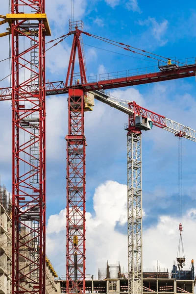 Several red cranes have been put to work on the construction of a modern multi-storey residential complex against a blue sky with white clouds. Concept work for builder. Outdoors. Sunny day.