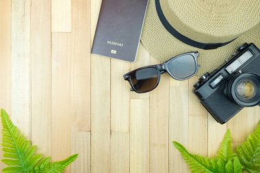Gerekli seyahat aksesuarları, tropikal yaprak alanı olan ahşap arka plan üzerinde öğeleri. Seyahat tatil kavramı düz moda stil, üstten görünüm yatıyordu.