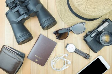 Gerekli seyahat aksesuarları, tropikal yaprak alanı olan ahşap arka plan üzerinde öğeleri. Seyahat tatil kavramı düz moda stil, üstten görünüm yatıyordu.