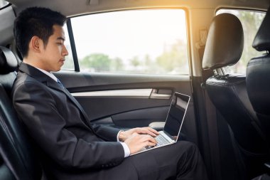 Dizüstü bilgisayar kullanarak ve geri araba koltuğunda oturan yakışıklı genç işadamı